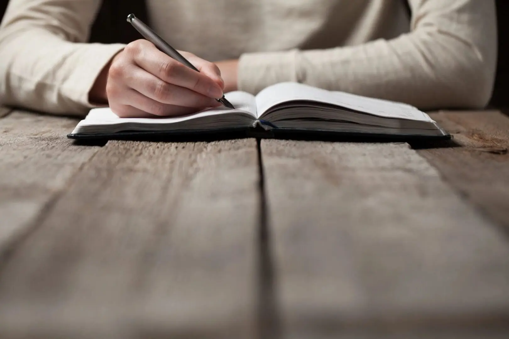 A man writing on a notebook on a wooden table